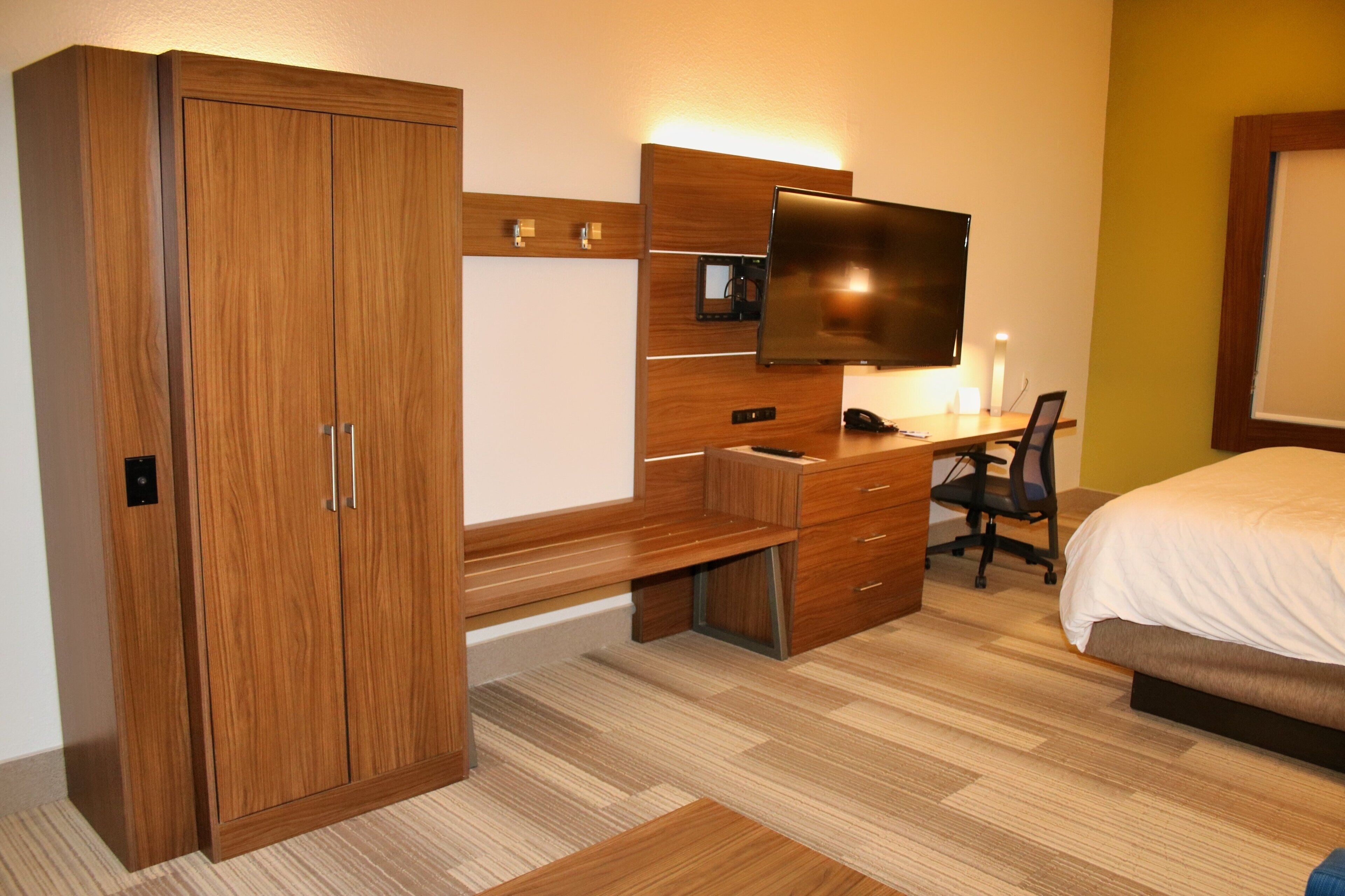 A hotel room with a wooden wardrobe, a desk with a flat-screen TV, a bed, and a chair.