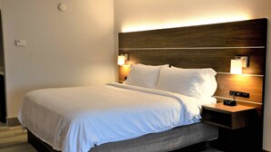 A neatly made bed with white linens, a wooden headboard, bedside lamps, and a small nightstand with a clock. - Holiday Inn Express & Suites Douglas by IHG (Douglas)
