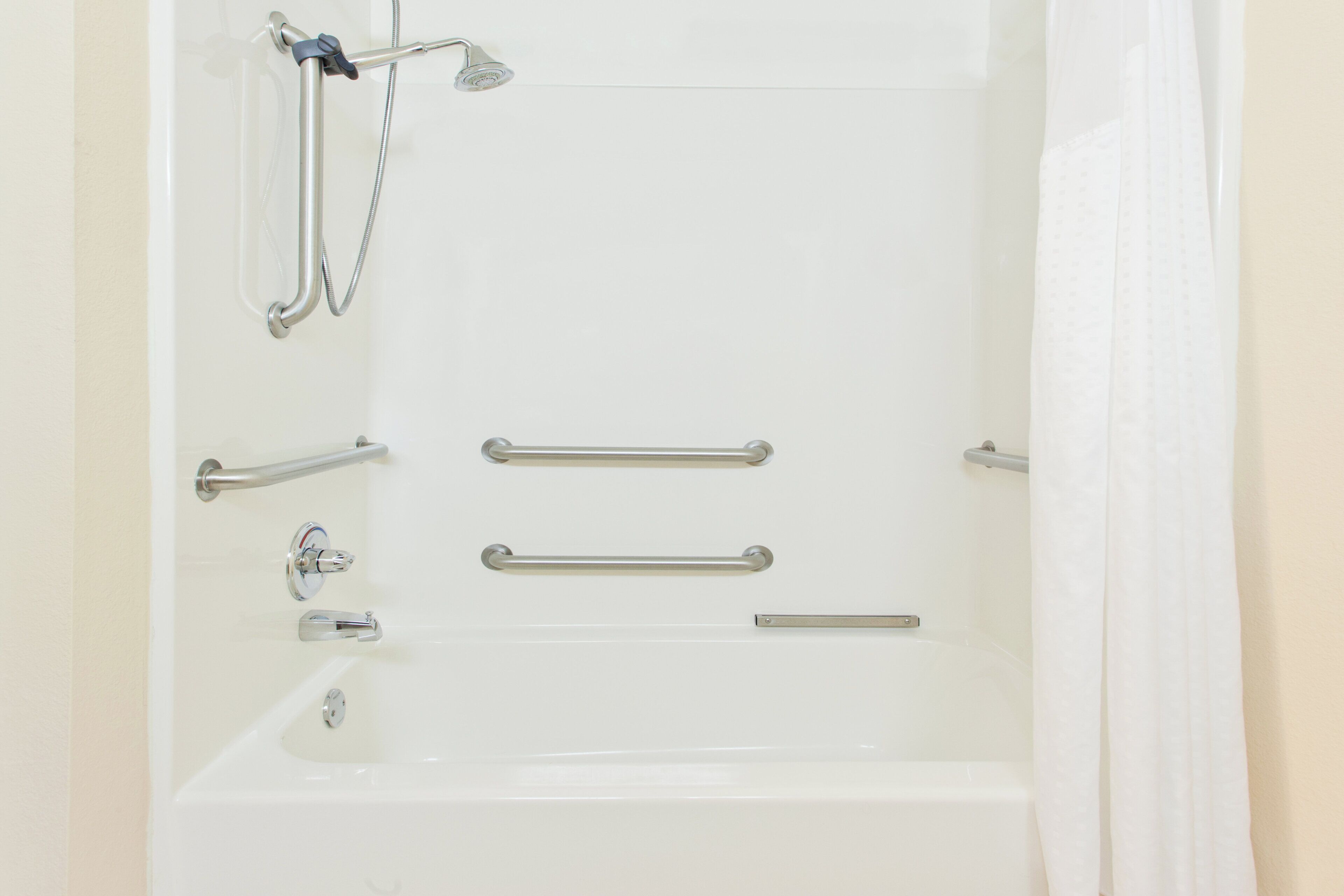 Una bañera blanca con cabezal de ducha, barras de apoyo y un grifo.