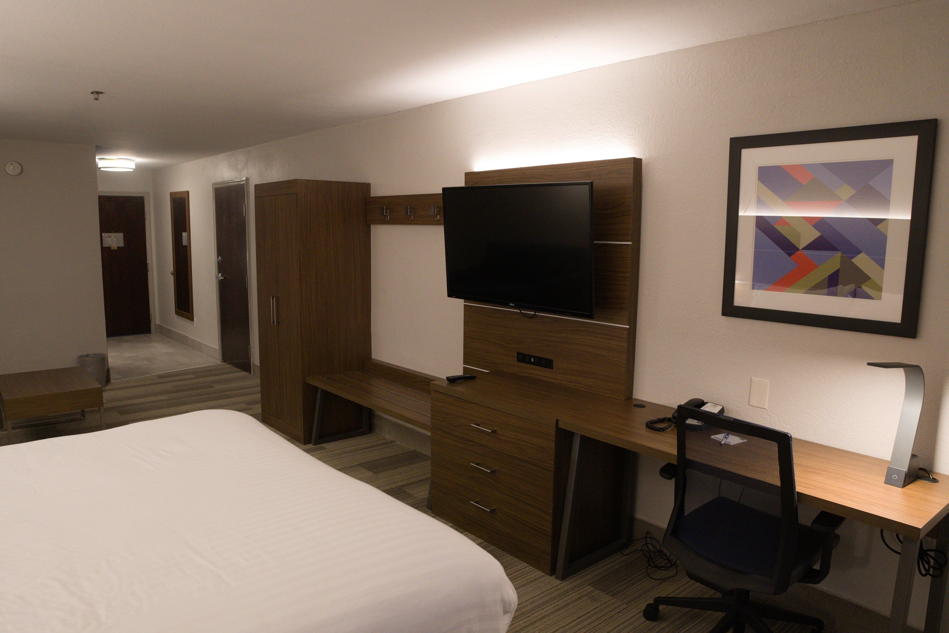A hotel room with a bed, a desk with a computer, a TV, and a framed picture on the wall.