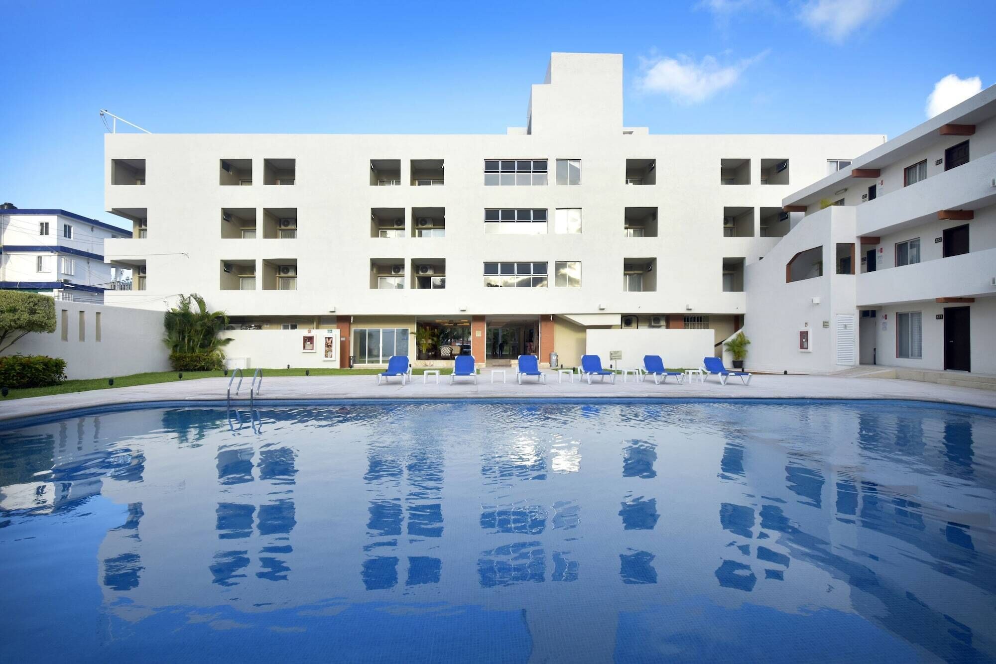 A modern building with a swimming pool, multiple balconies, and a clear sky.