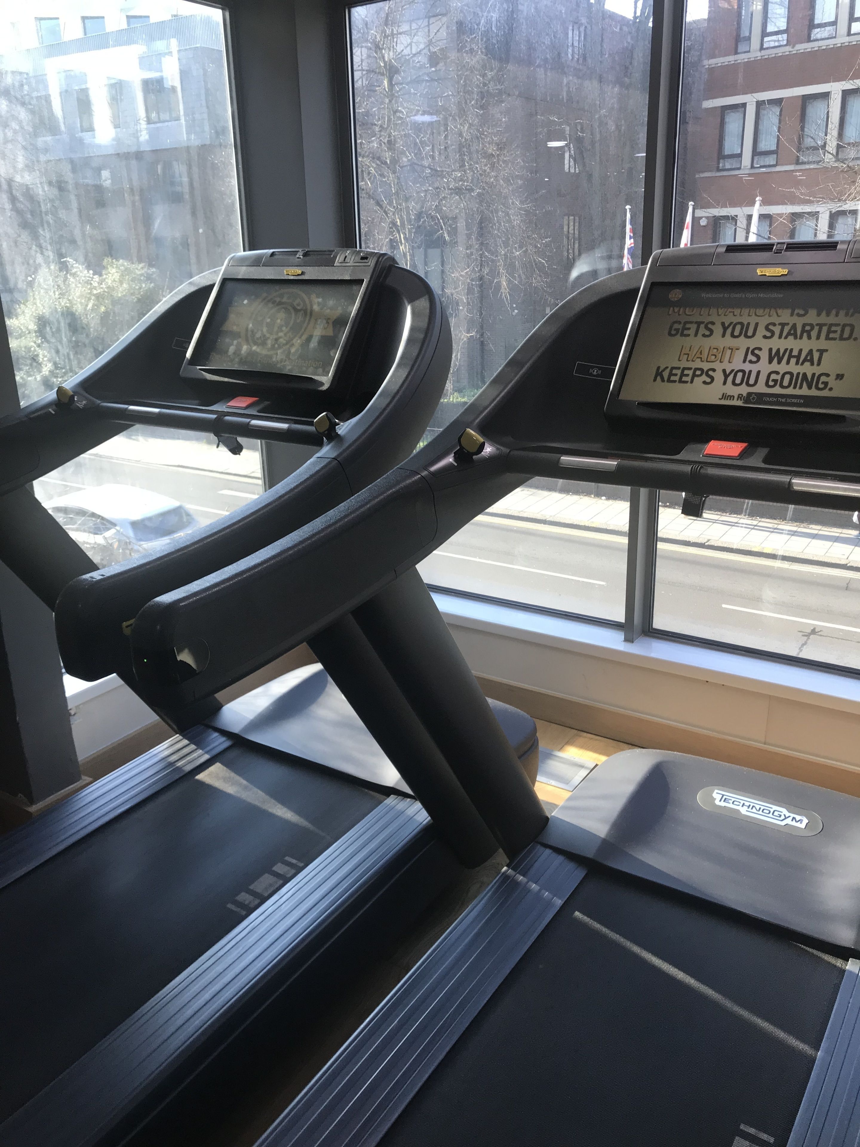 A treadmill with a motivational quote on the console, a window with a view of buildings and trees, and a door with a red handle.