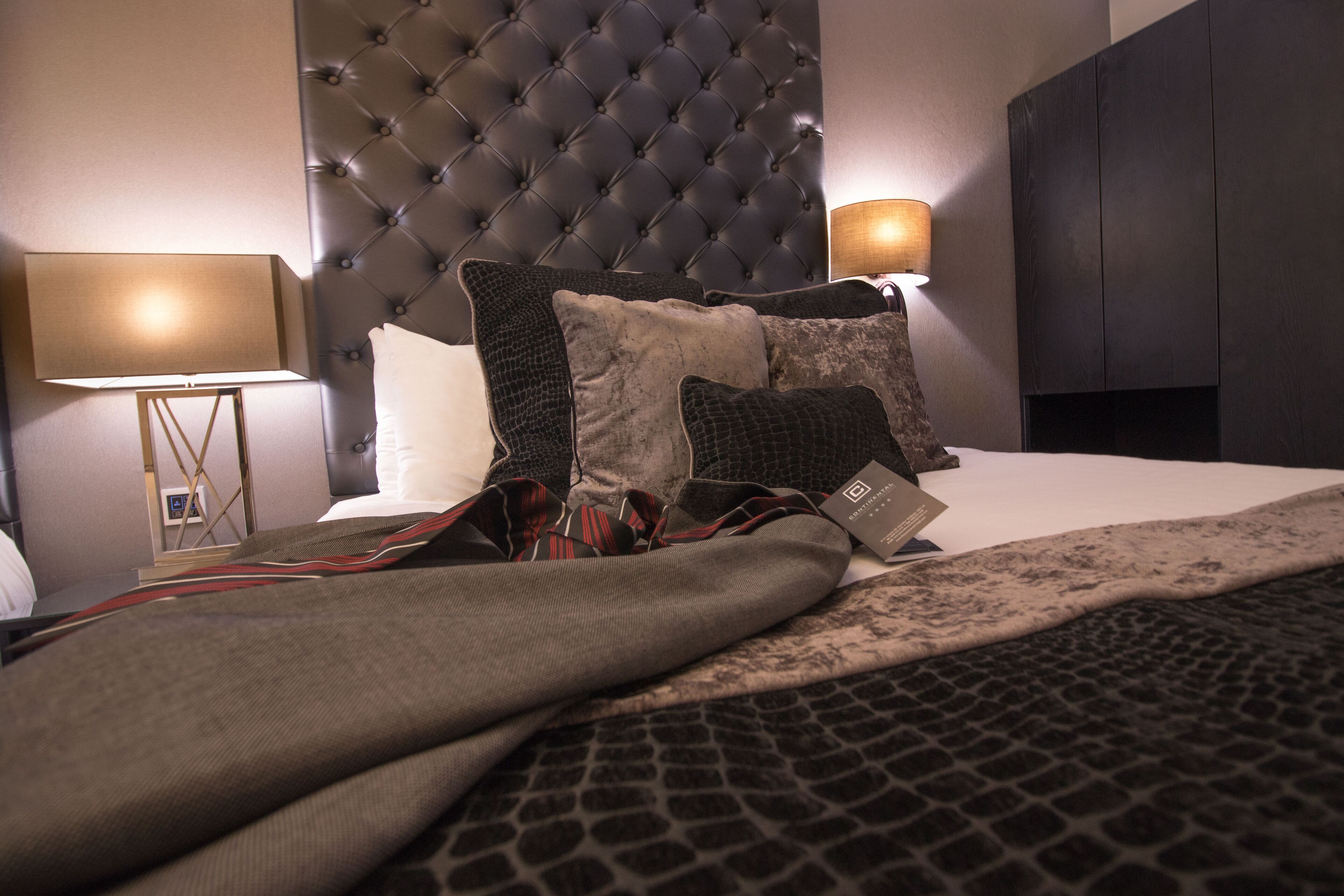 A neatly made bed with a tufted headboard, two bedside lamps, and a variety of pillows.