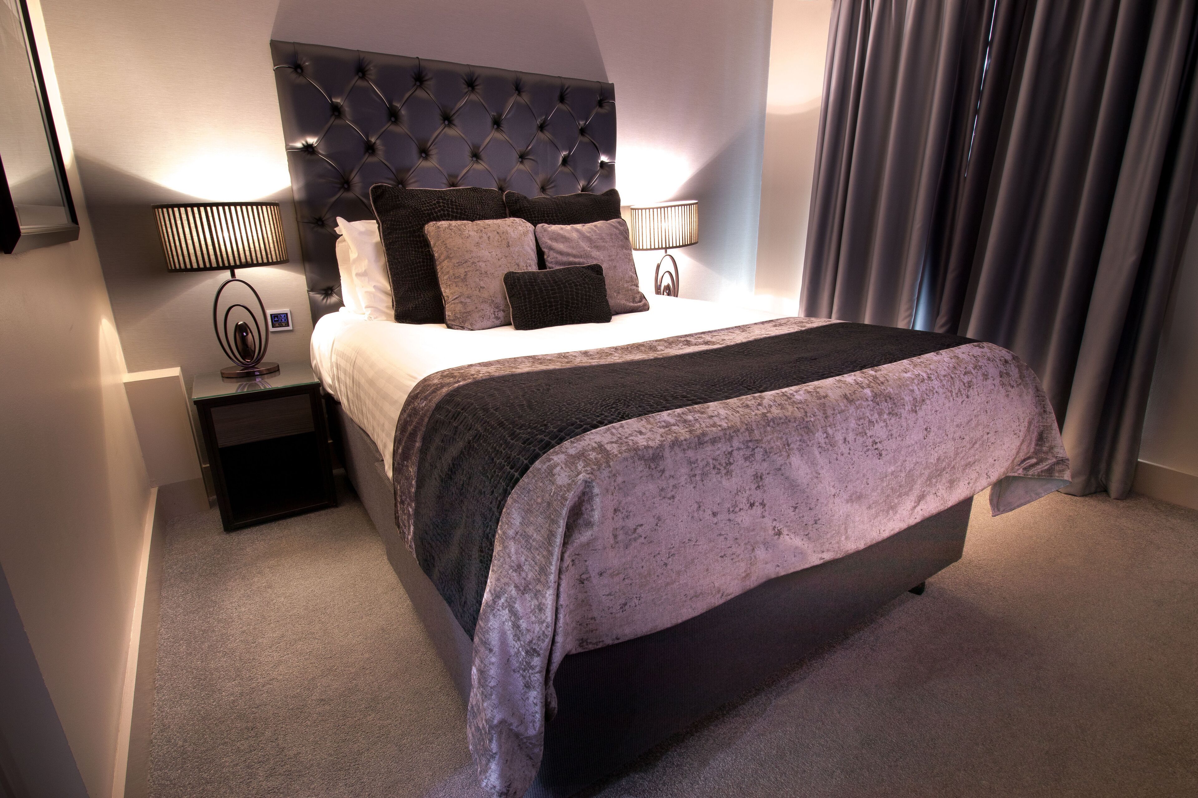 A neatly made bed with a tufted headboard, two bedside lamps, and a small nightstand.