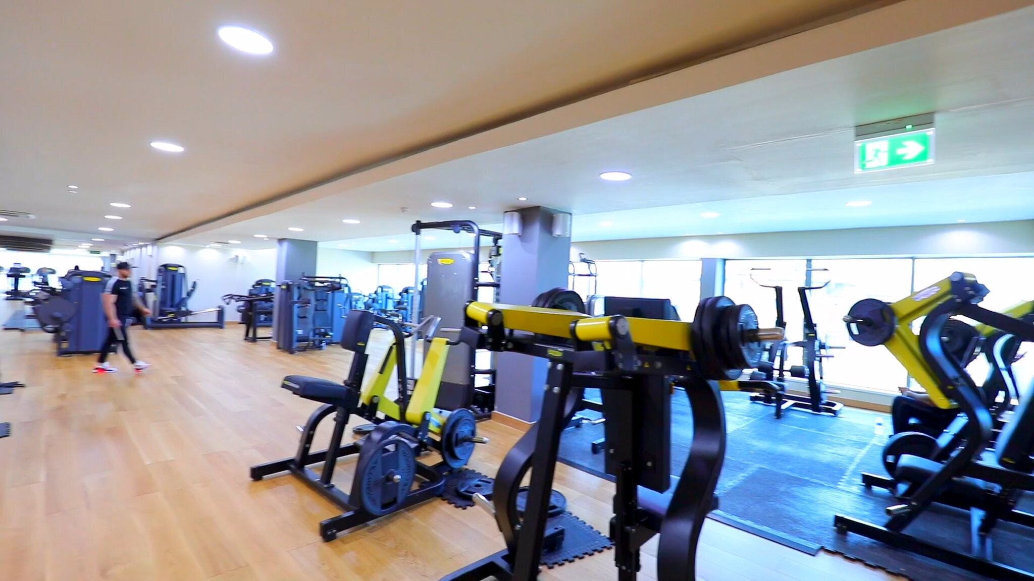 Een fitnessruimte met diverse trainingsapparaten, houten vloeren en een spiegelwand.