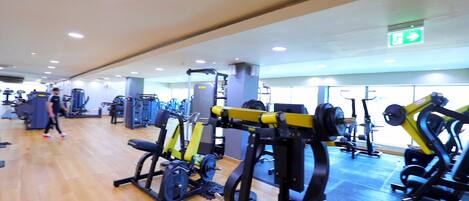 A gym with various exercise machines, wooden flooring, and a mirrored wall.