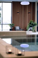 A modern indoor pool area with a seating area, wooden panel walls, and potted plants.