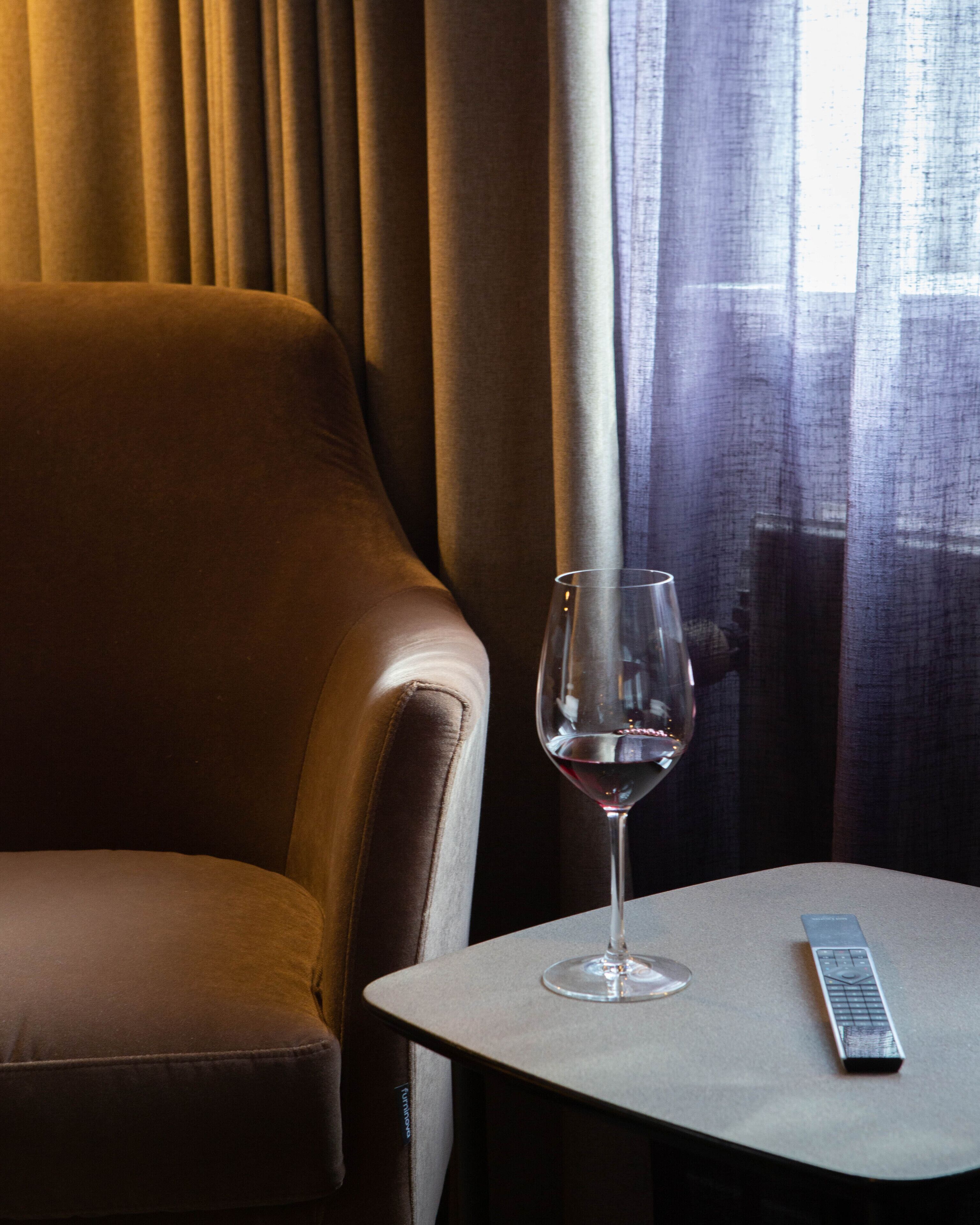 Un sillón de cuero, una copa de vino tinto y un control remoto sobre una mesita.
