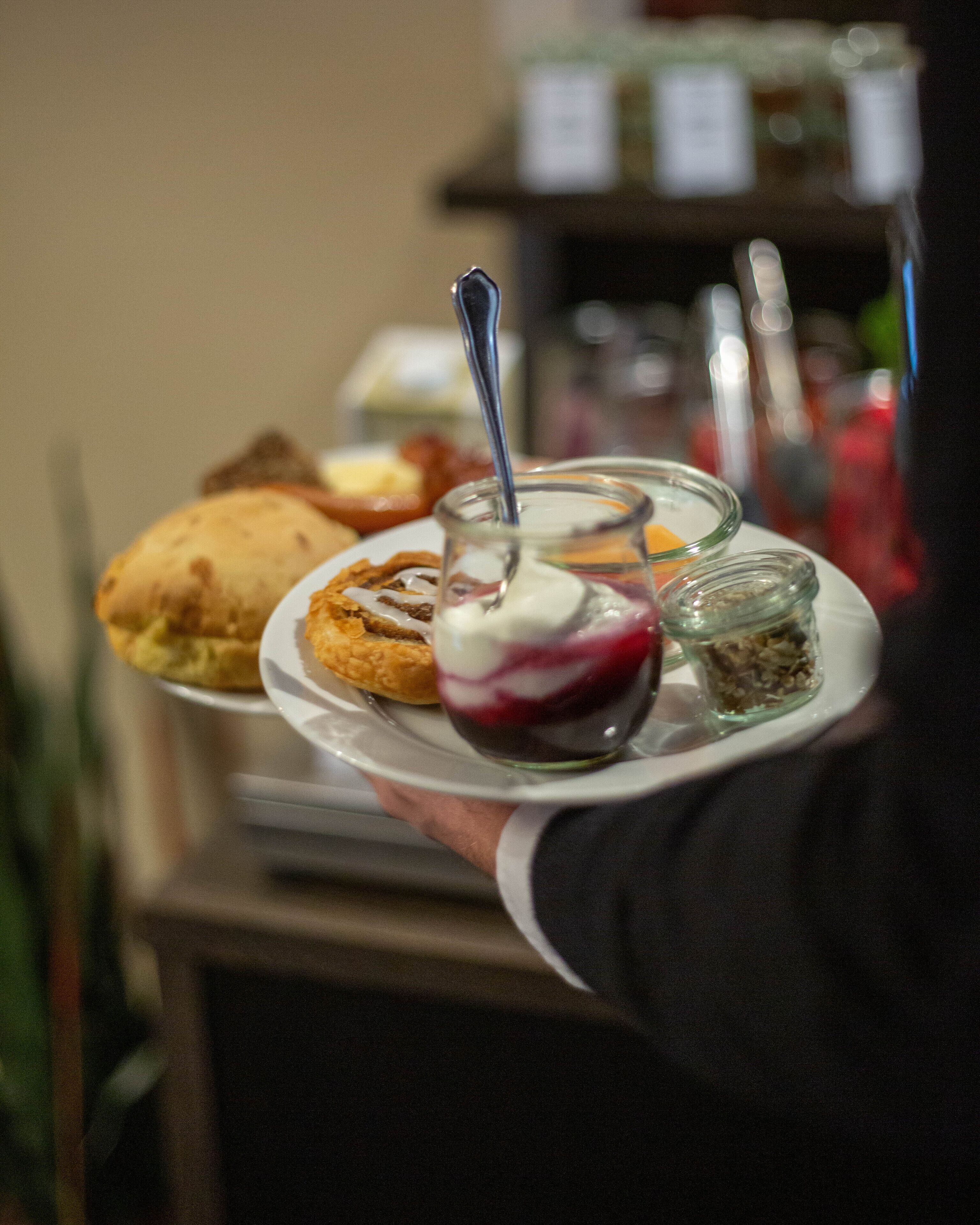A tray with a pastry, a dessert with a spoon, and a small jar of what appears to be a condiment or topping.
