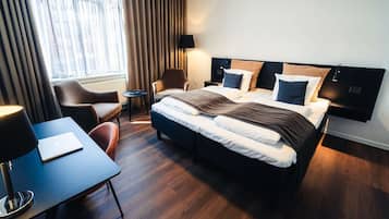 Een moderne hotelkamer met een groot bed, een bureau met een laptop, een stoel en een raam met gordijnen.