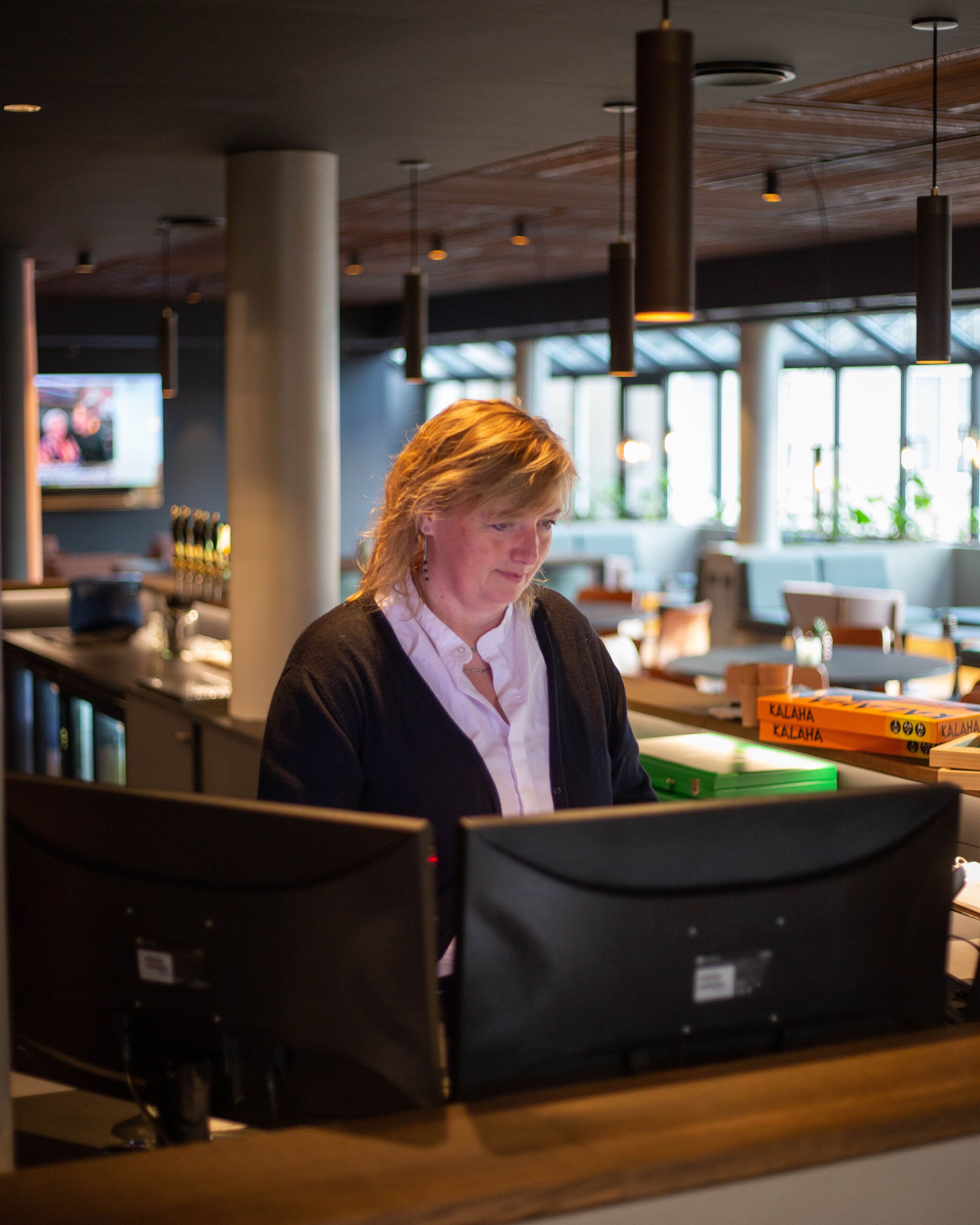 A person working at a counter in a modern indoor setting with large windows and hanging lights.