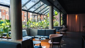 A modern indoor space with a glass ceiling, green plants, and seating areas. - Grand Hotel Struer (Struer)
