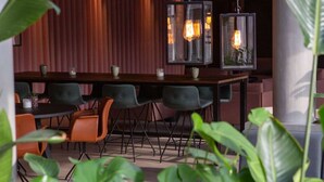 A modern dining area with a long table, multiple chairs, hanging pendant lights, and potted plants. - Grand Hotel Struer (Struer)