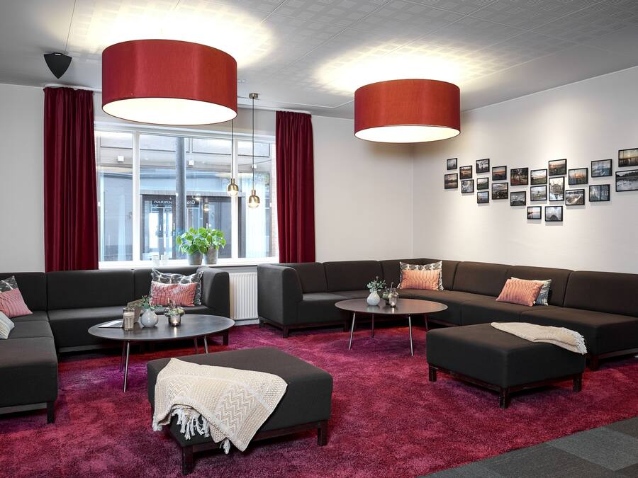 Una sala de estar moderna con un sofá seccional, un reposapiés y una mesa de centro. Hay cortinas rojas, un ventanal grande y una pared llena de cuadros.