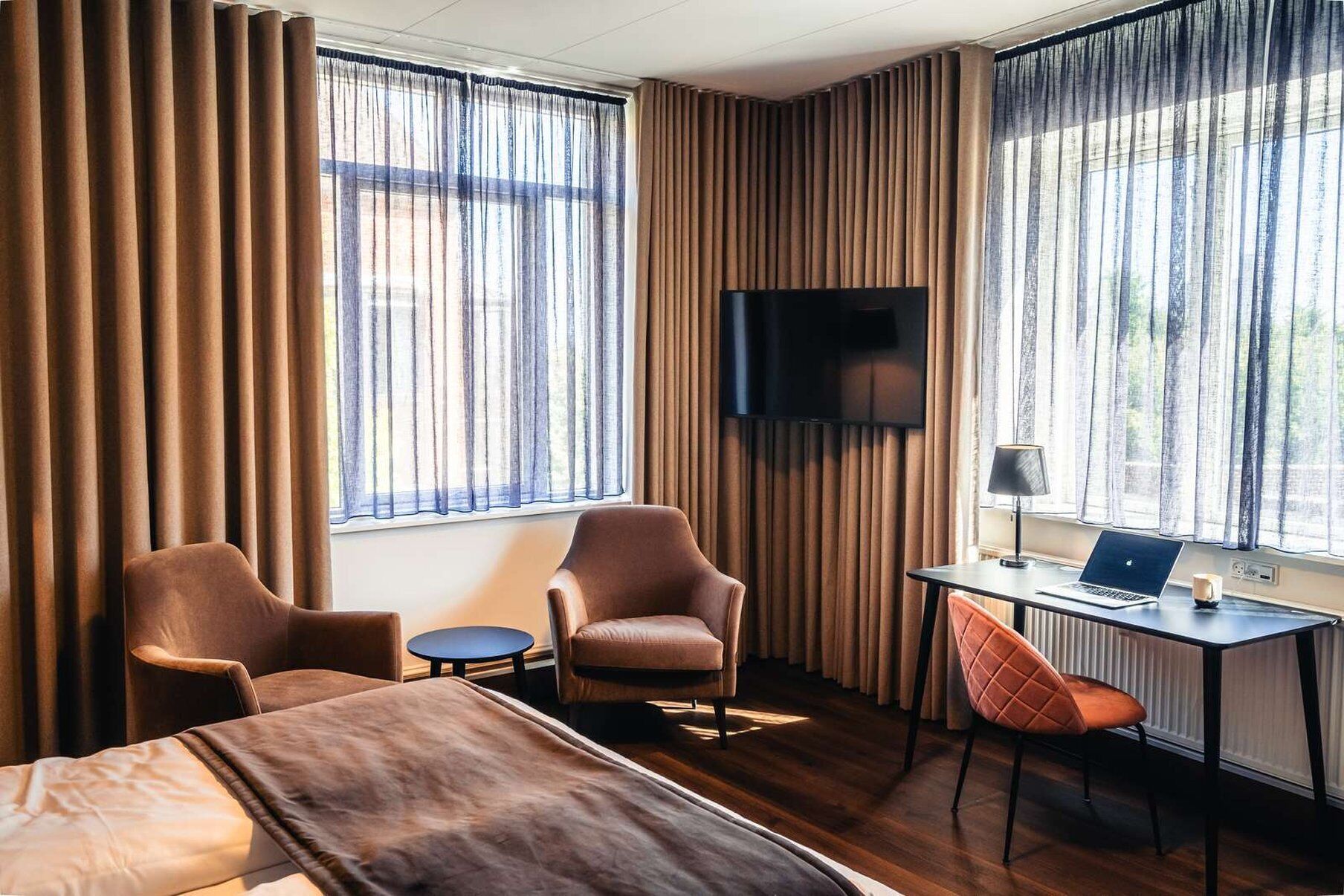 Habitación de hotel con una cama, dos sillones, un escritorio con una computadora portátil y un televisor montado en la pared.