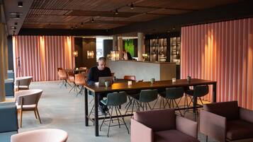 A modern lounge area with a long table, multiple chairs, and a bar in the background.
