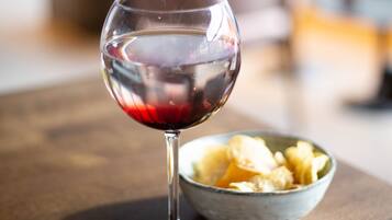 A glass of red wine on a wooden table with a bowl of snacks beside it.