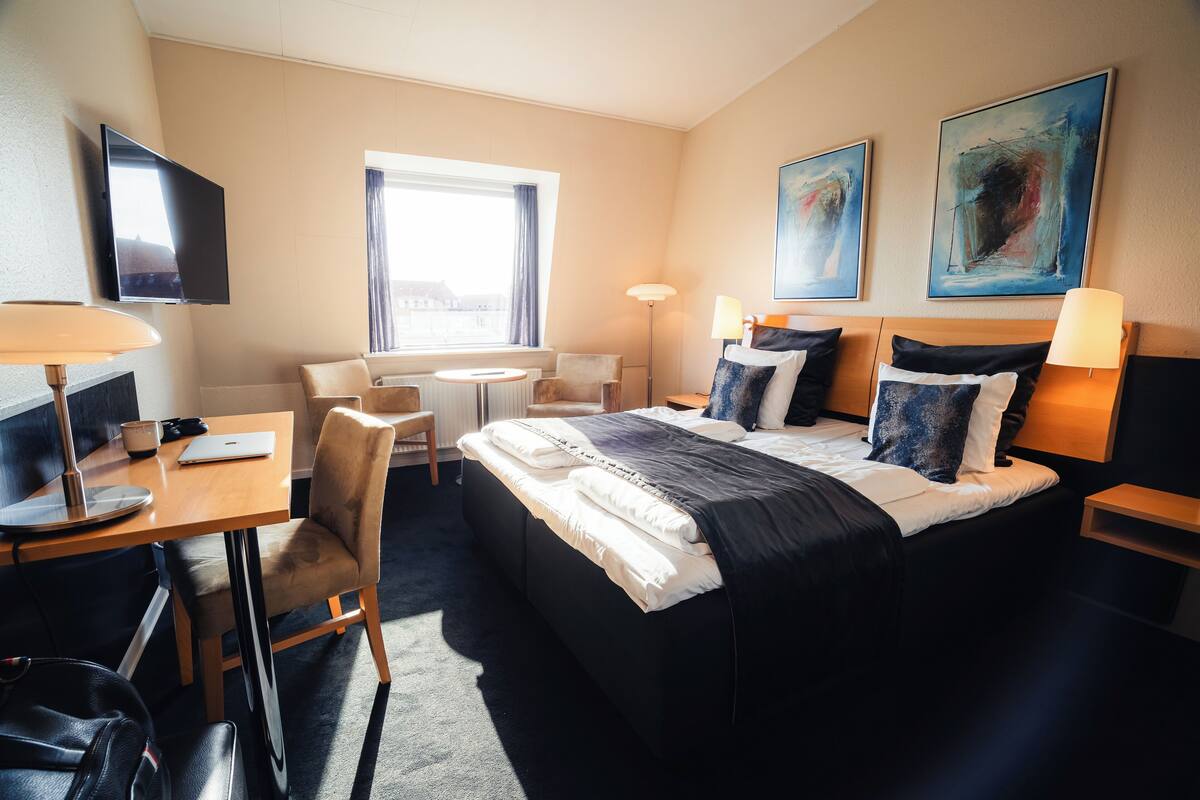 A hotel room with a bed, desk, chair, and a TV.