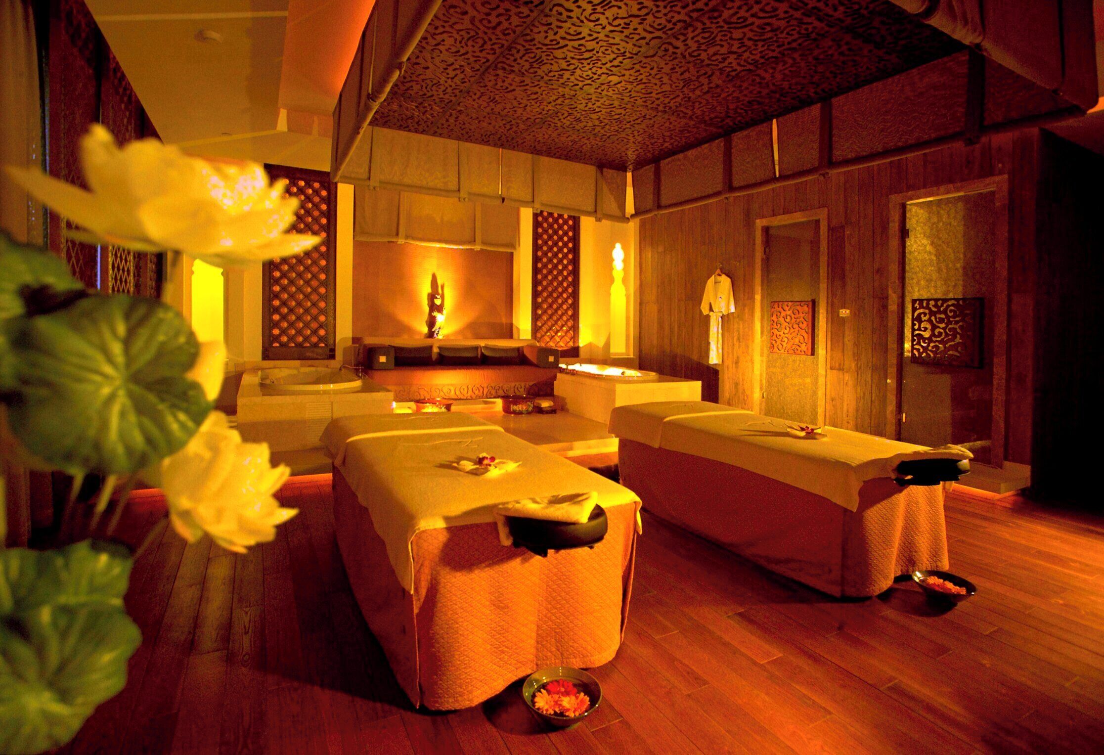 A spa room with two massage tables, a wooden floor, and a decorative wall.