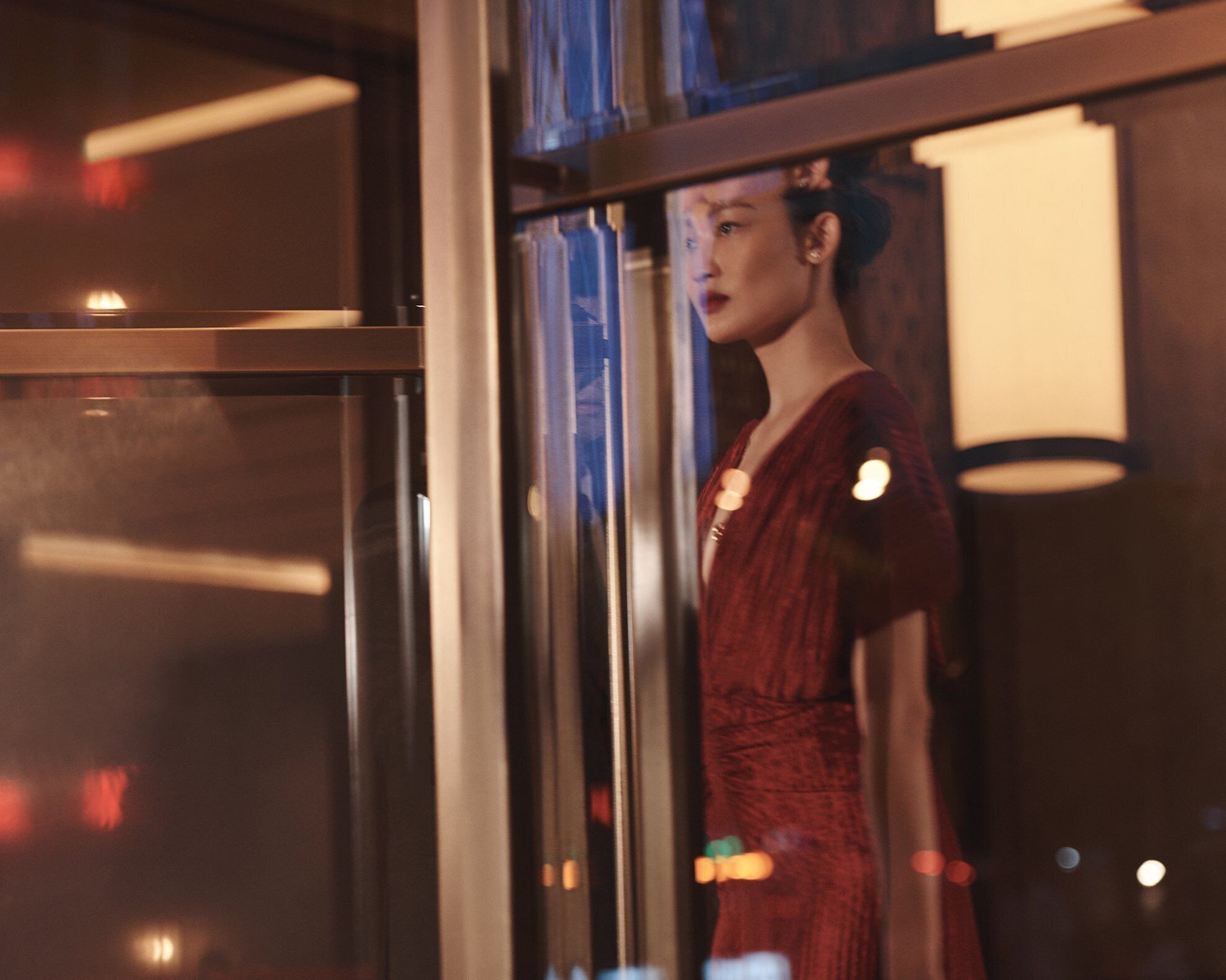 A mannequin in a red dress inside a room with a glass door, a wooden floor, and a visible window.