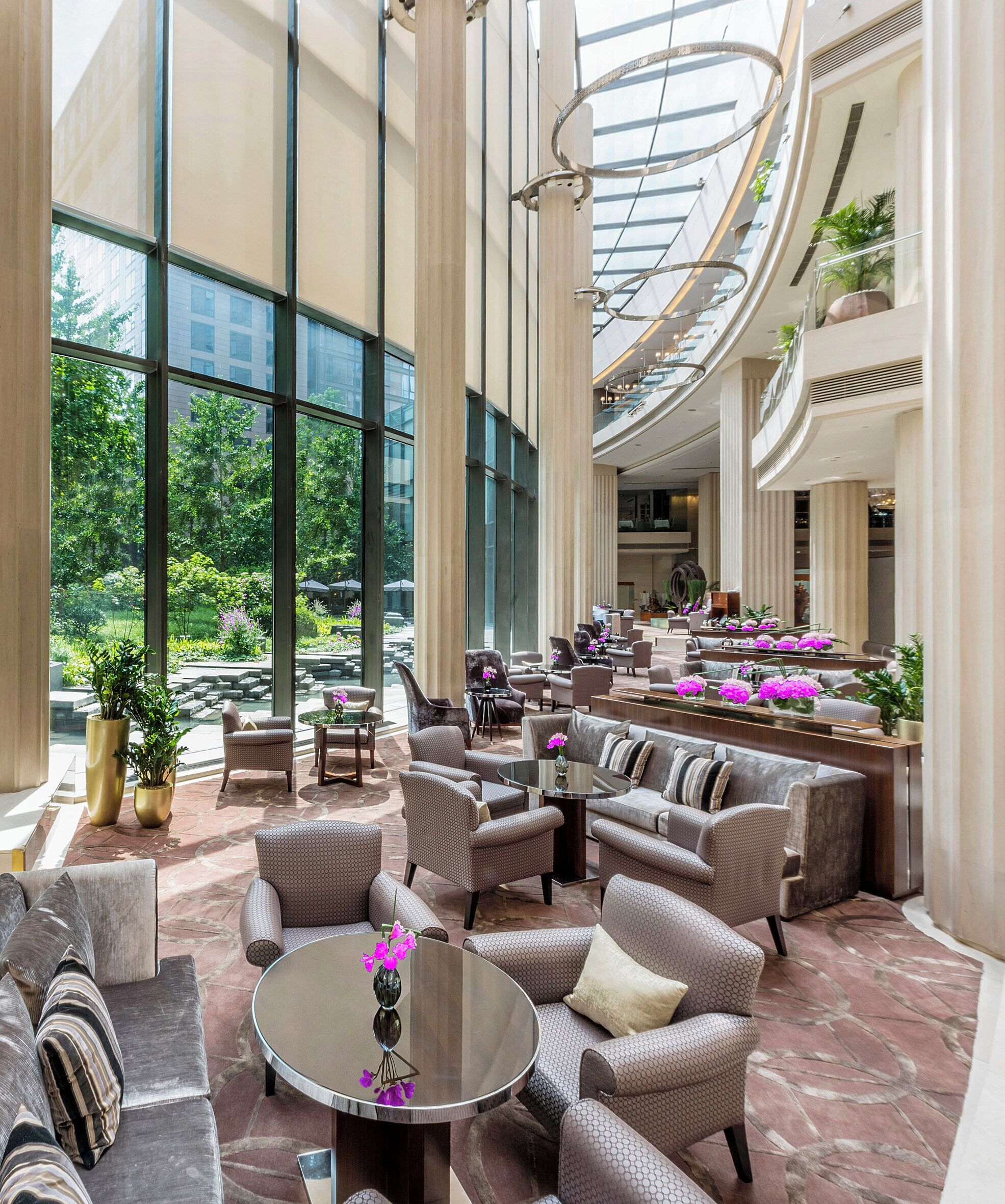 A spacious lobby with high ceilings, large windows, and a central seating area with sofas and armchairs.