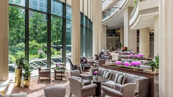 A spacious lobby with high ceilings, large windows, and a central seating area with sofas and armchairs.
