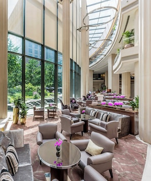 A spacious lobby with high ceilings, large windows, and a central seating area with sofas and armchairs.