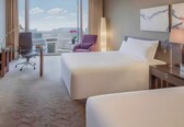 A hotel room with two beds, a desk with a chair, a lamp, and a view of the city.