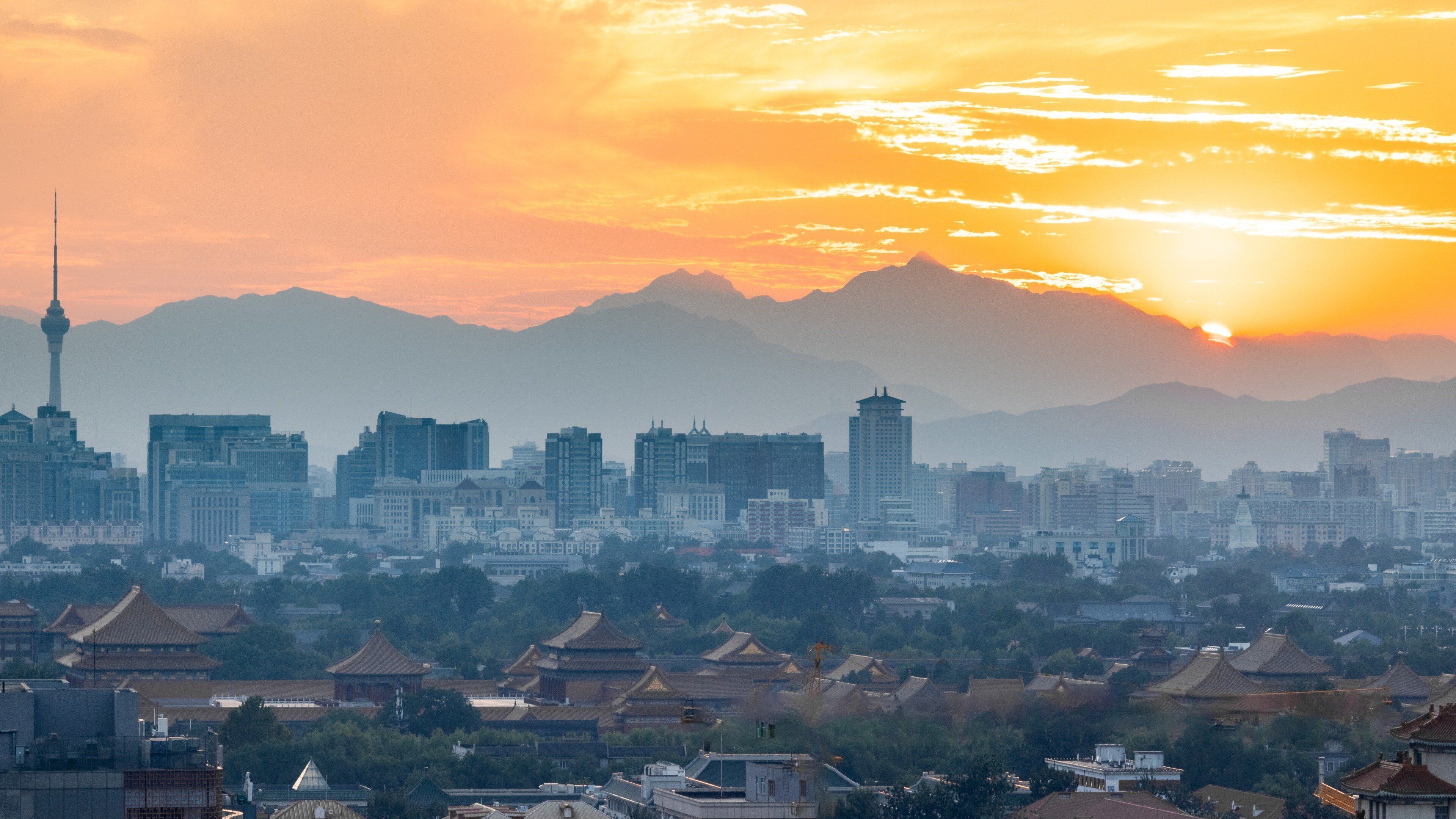 A cityscape with traditional architecture in the foreground and modern buildings in the background, under a sunset sky.