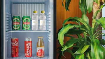 A mini-fridge with beverages including soda cans, water bottles, and a bottle of apple juice.