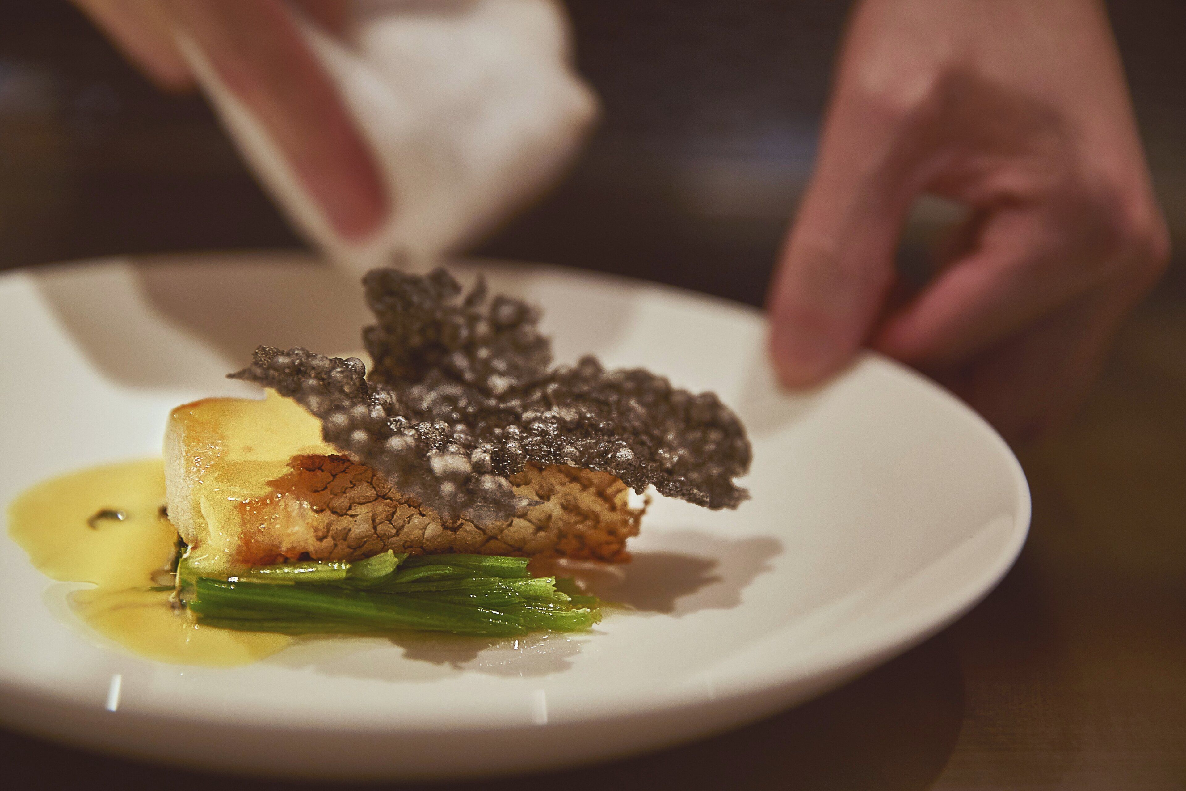A plate with a piece of meat, green vegetables, and a sauce.