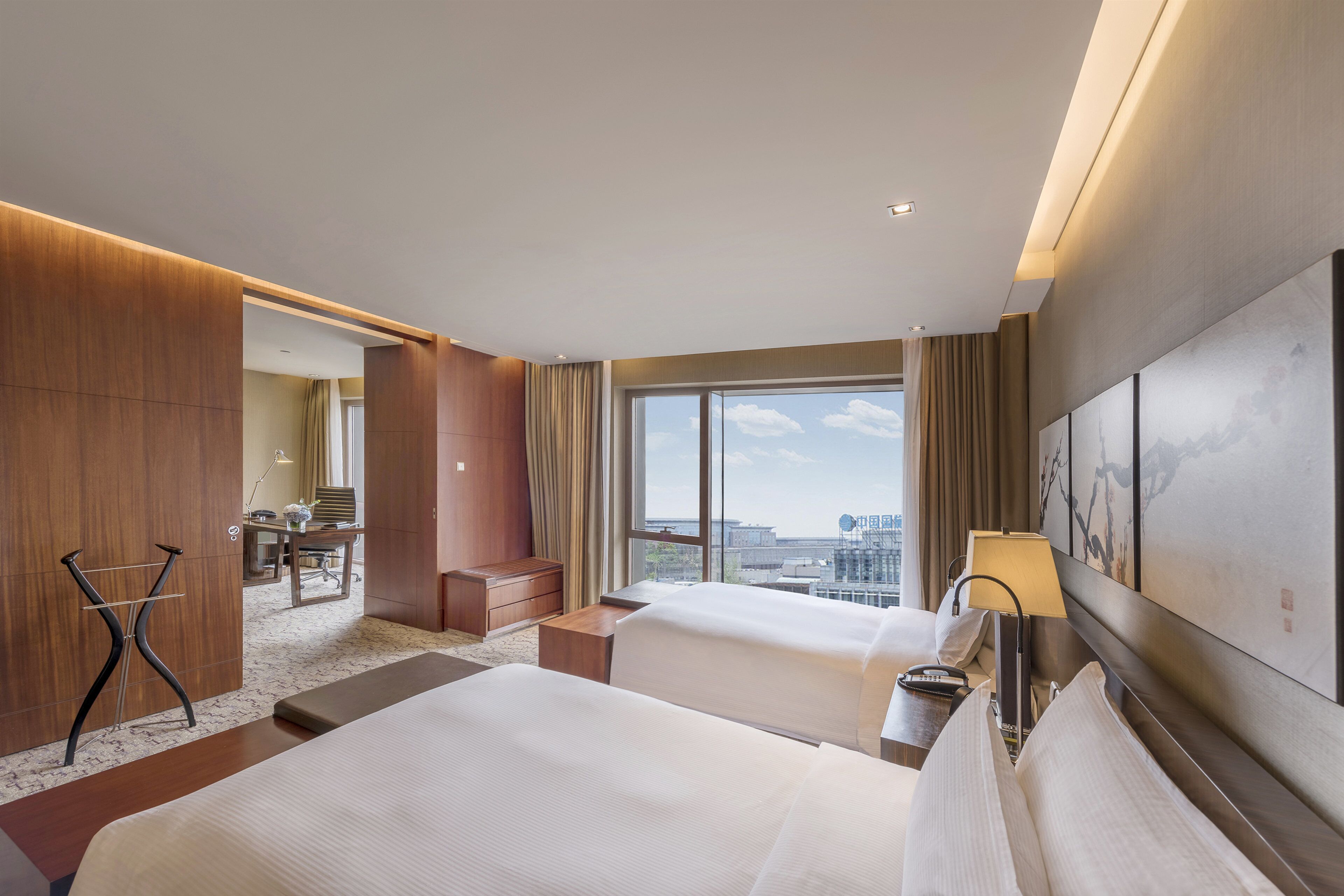 A hotel room with two beds, a desk, and a view of the city.