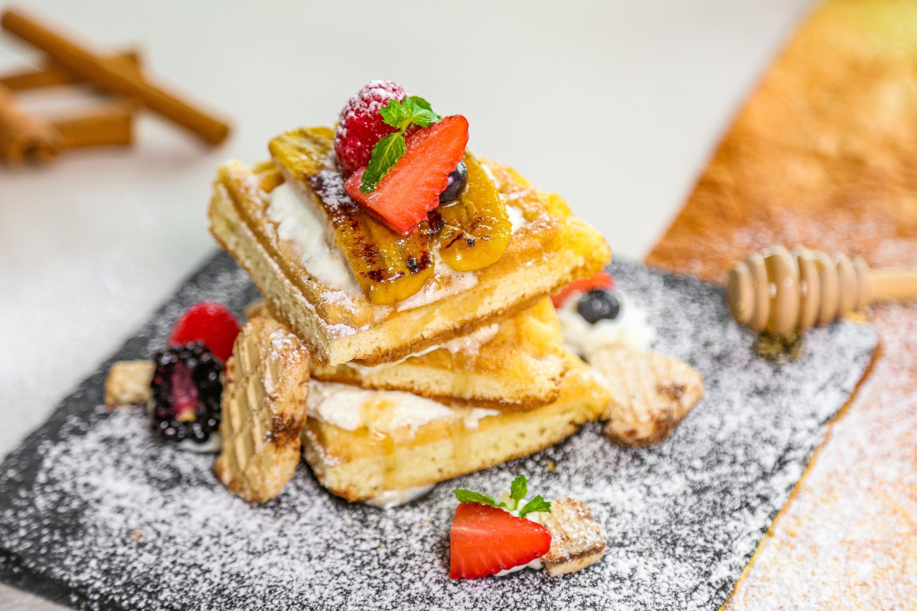 A stack of pancakes with fruit toppings and powdered sugar.