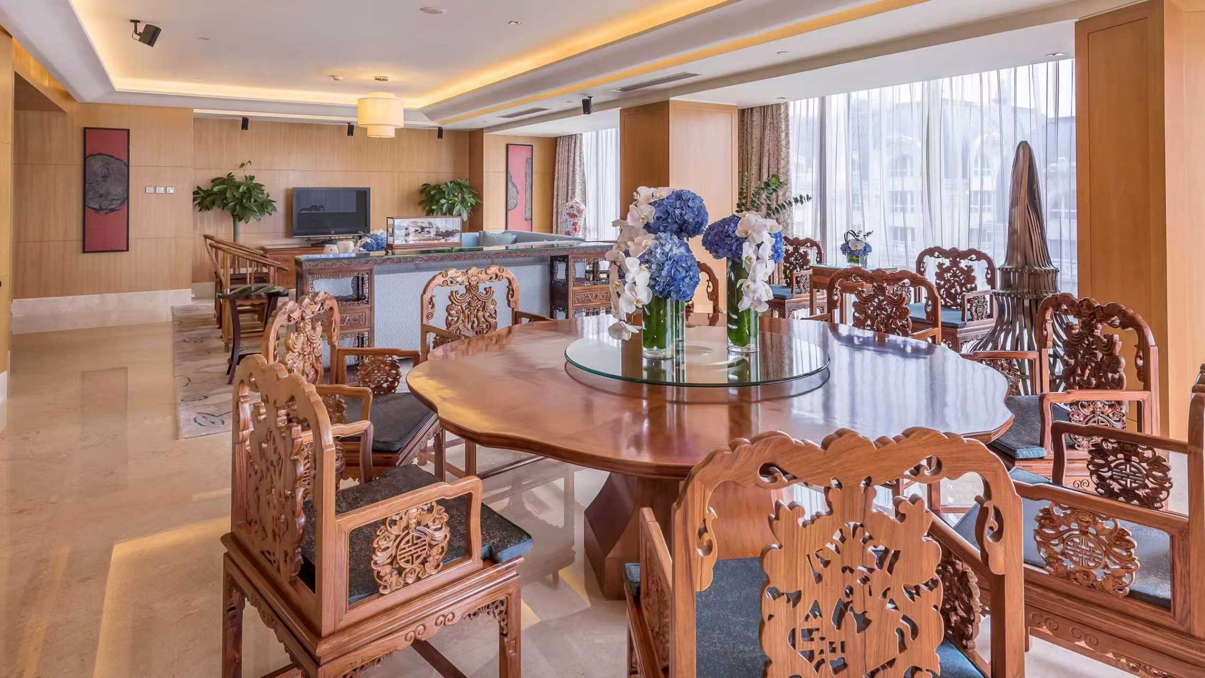 A spacious dining area with a round table, ornate wooden chairs, and a television in the background.