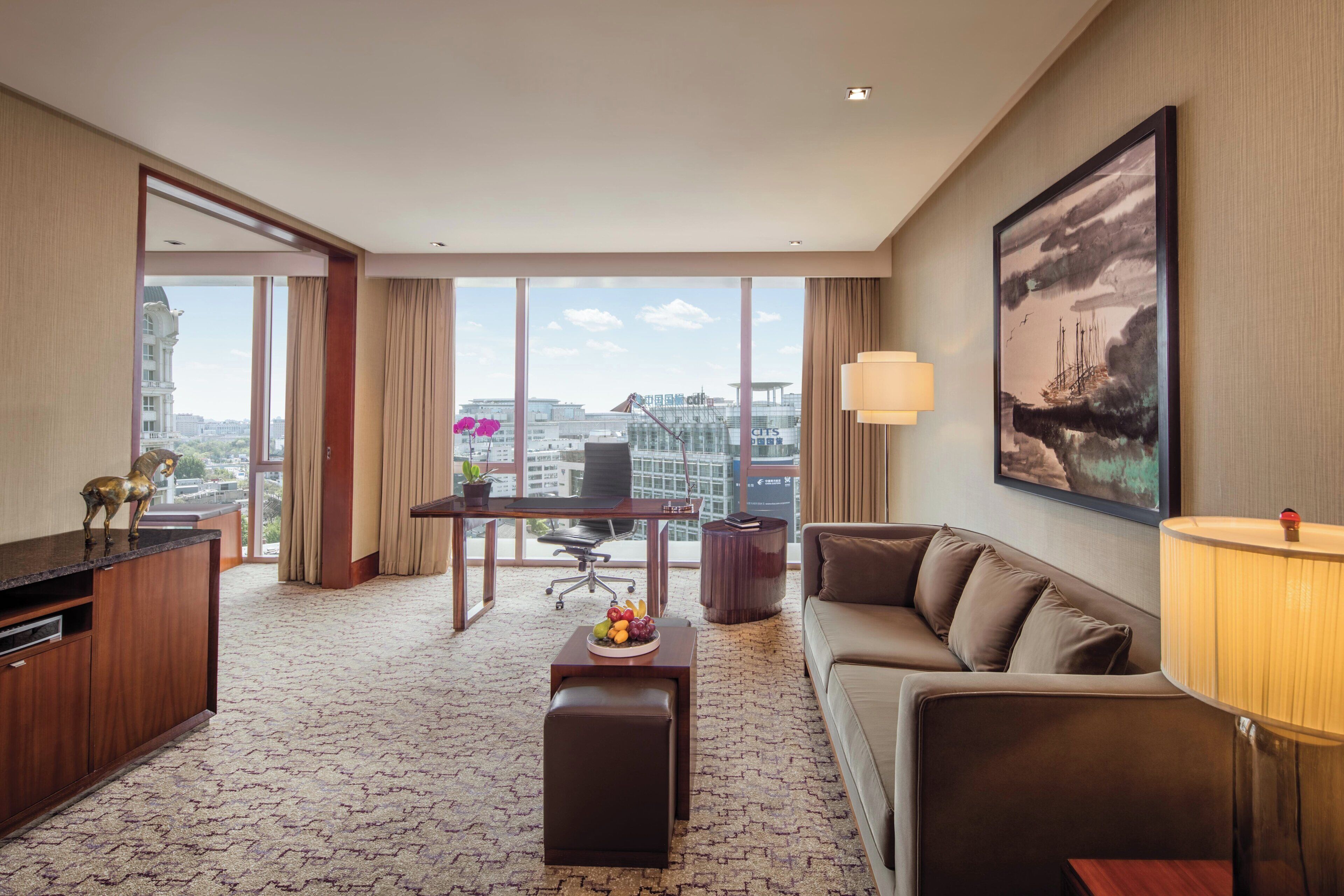 Una habitación de hotel con un ventanal grande, un sofá, un escritorio y una mesa de comedor.
