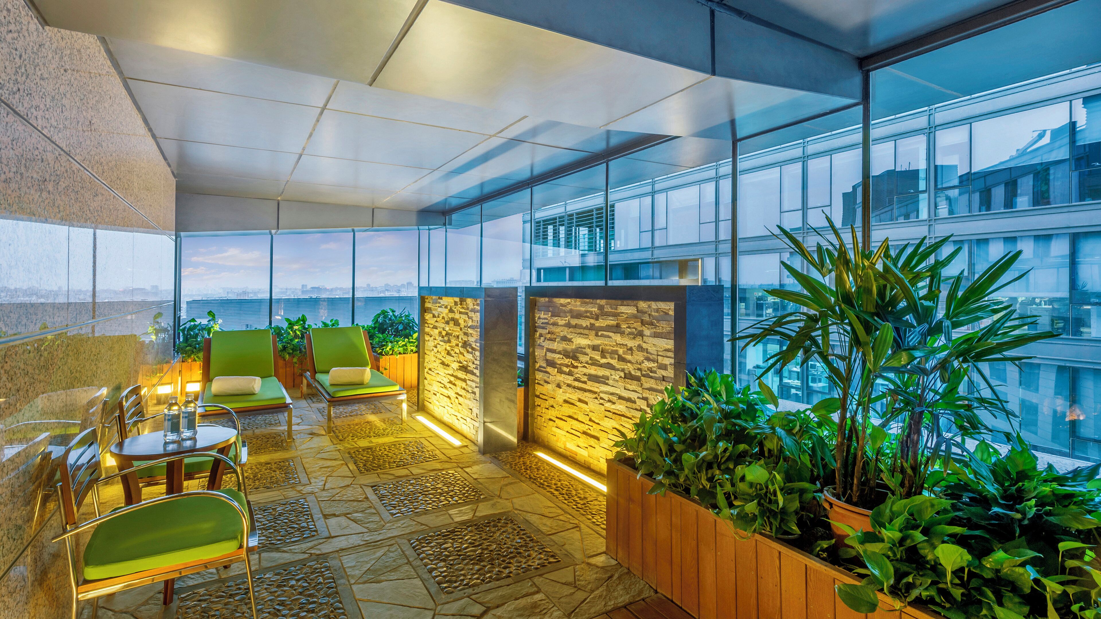 Un espace intérieur moderne, doté de sièges, d’un sol en pierre et de grandes fenêtres offrant une vue sur la ville.