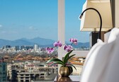 A cityscape view from a window with a vase of purple orchids on a table.