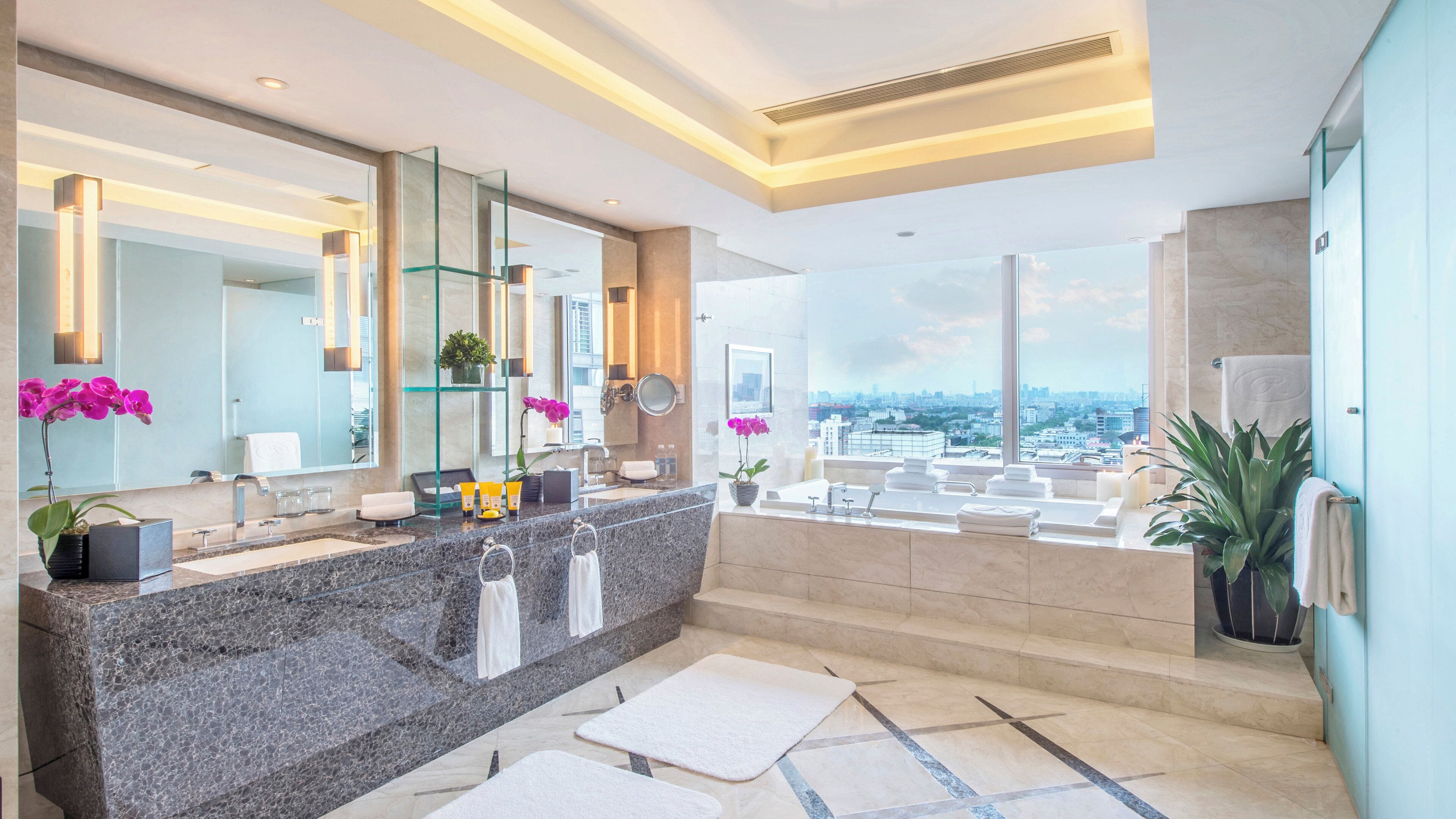 A modern bathroom with a granite countertop, multiple sinks, a large mirror, and a city view.