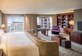 A hotel room with a large bed, a sofa, a desk, a chair, a bookshelf, and a television.