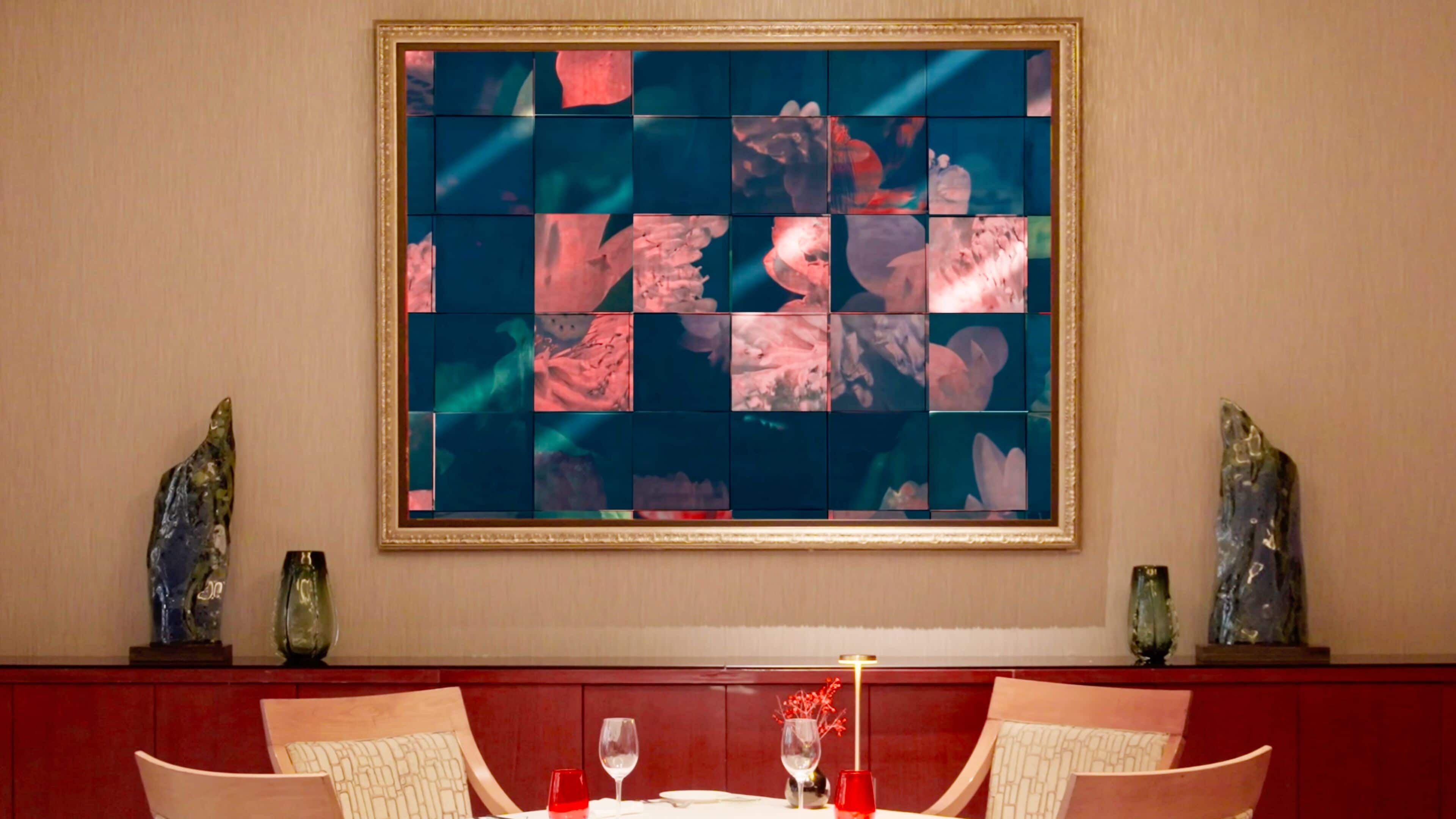 A dining area with a table set for two, a large abstract painting on the wall, and two decorative vases on either side of the table.