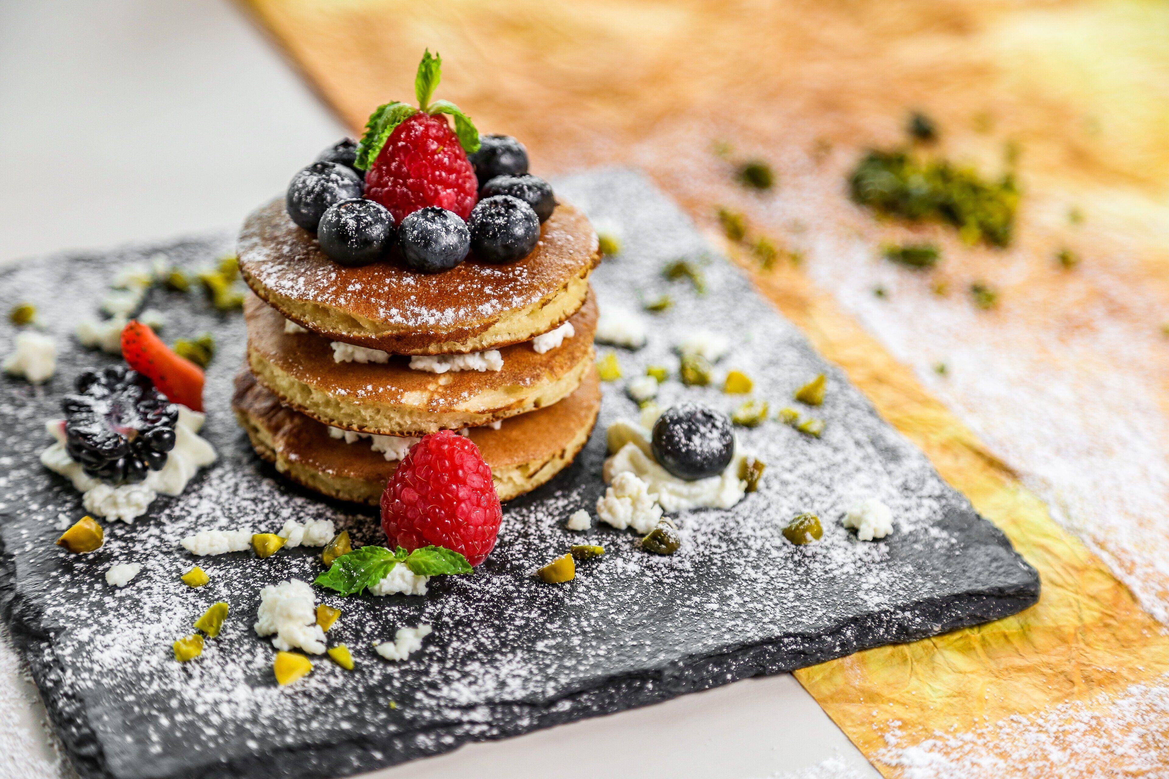 A stack of pancakes with berries and powdered sugar on a slate plate.