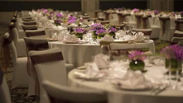 Ein Bankettraum mit runden Tischen, gedeckt für ein Essen, jeweils mit weißen Tischdecken und lila Blumen.