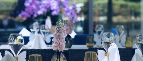 Una mesa de comedor preparada con copas de vino, un florero con flores y vistas a flores púrpuras a través de una ventana.