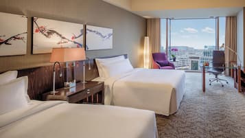 Habitación de hotel con dos camas, un escritorio, una silla y vistas a la ciudad.