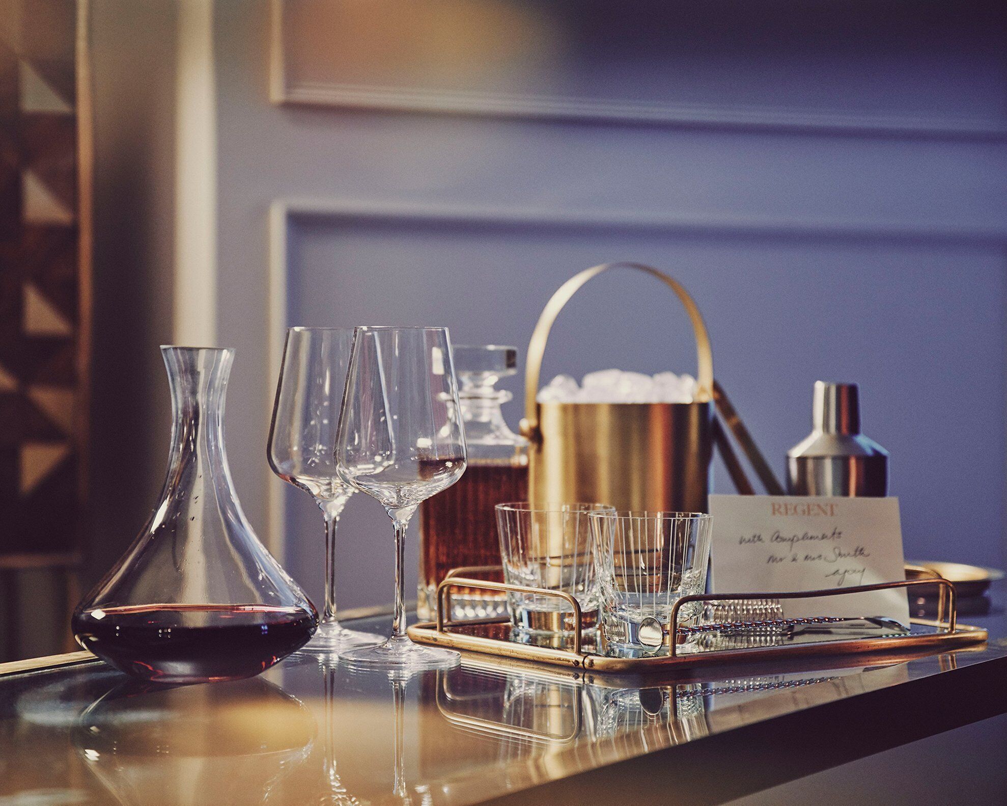 A bar setting with a wine bottle, glasses, a tray, and a sign.