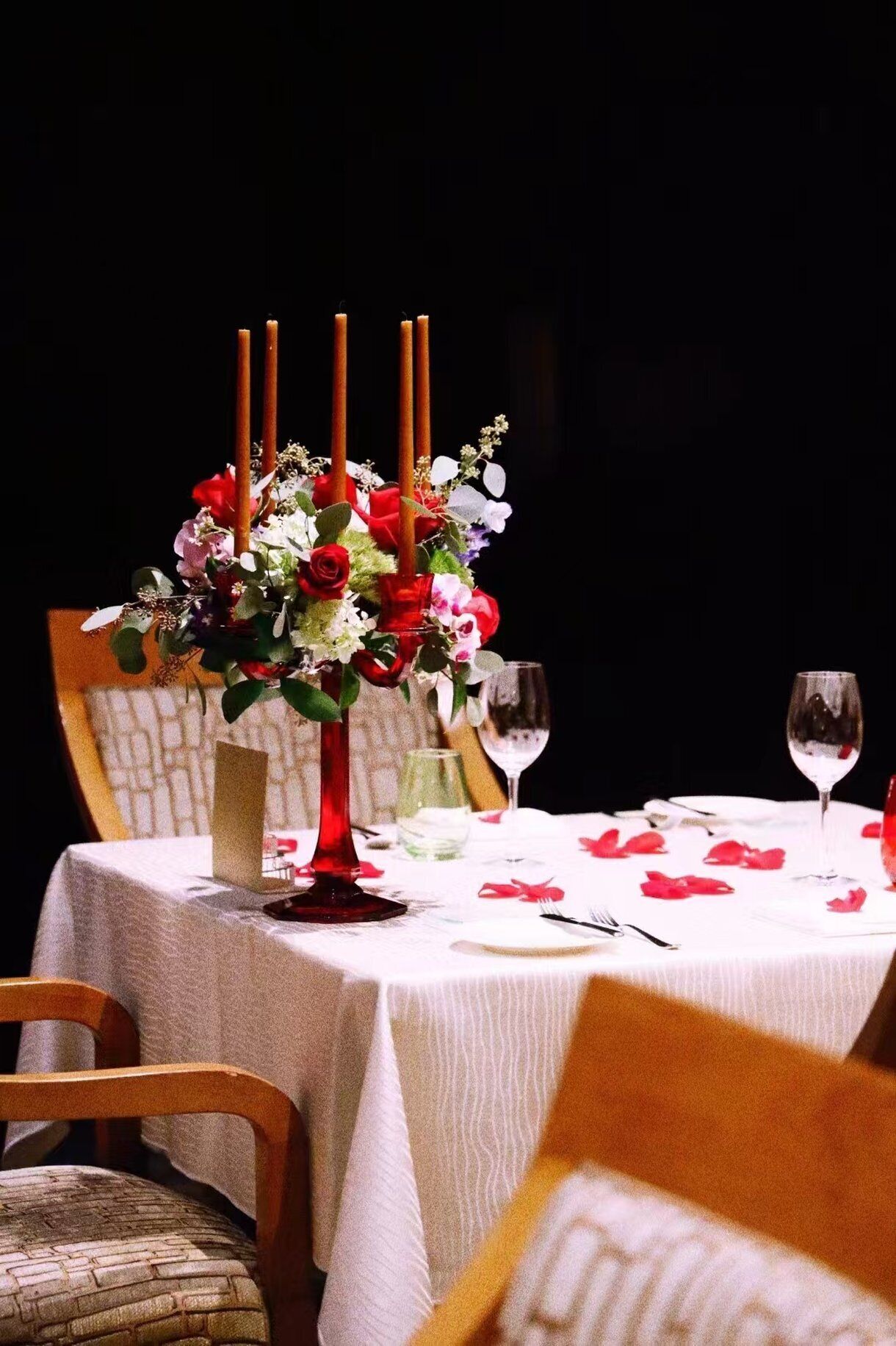 Mesa lista para comer, con un centro de flores y velas, una copa de vino y un menú.