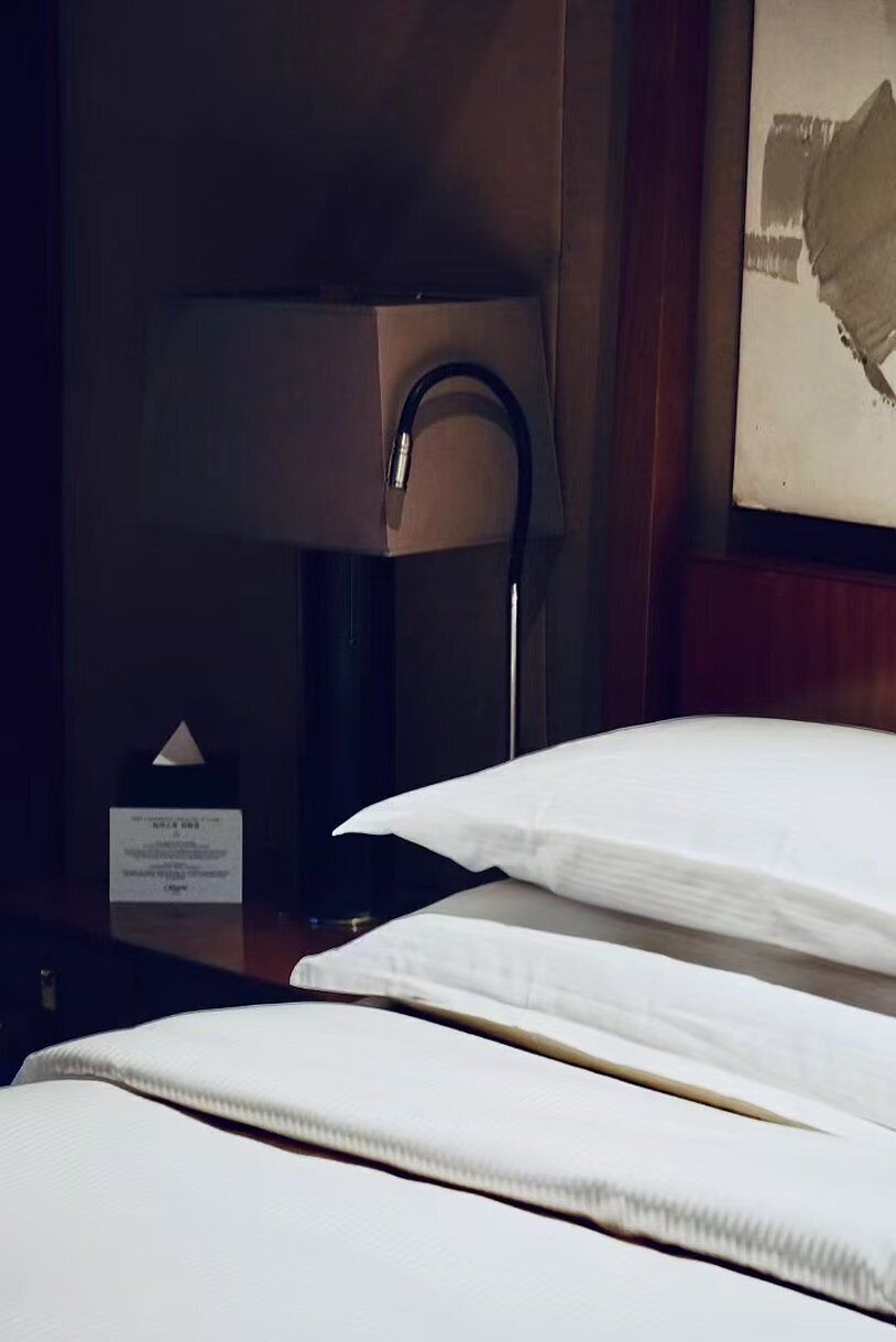 Una camera d'albergo con un letto rifatto, un comodino con una lampada e un quadro appeso al muro.