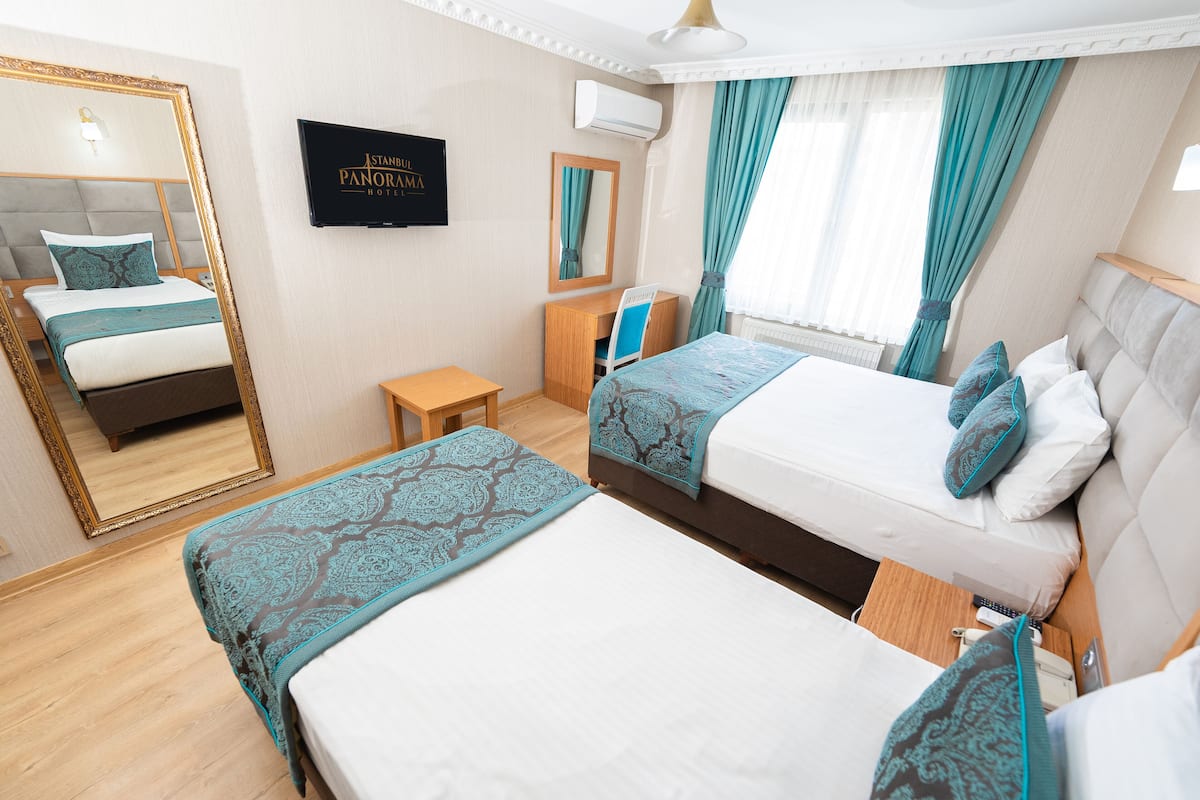 A hotel room with two beds, a TV, a mirror, and a window with curtains.
