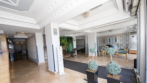 Un hall d’entrée spacieux avec un sol en marbre, un comptoir d’accueil et un espace détente avec des fauteuils verts.