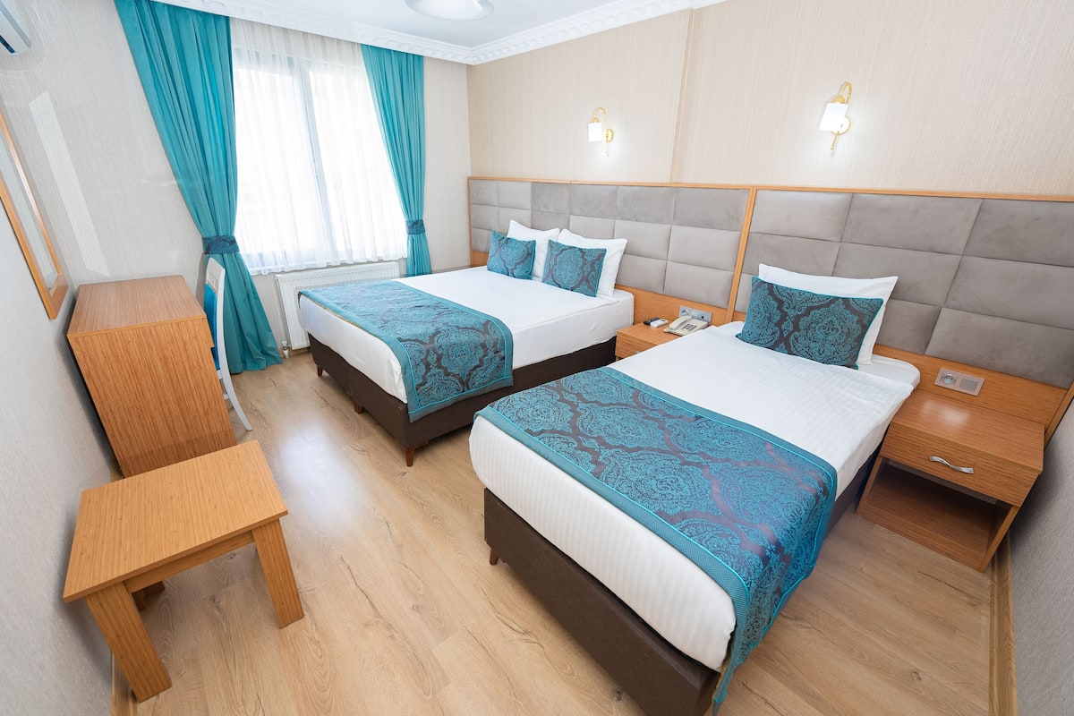 A hotel room with two beds, a wooden nightstand, a small wooden table, and a bedside table with a lamp.